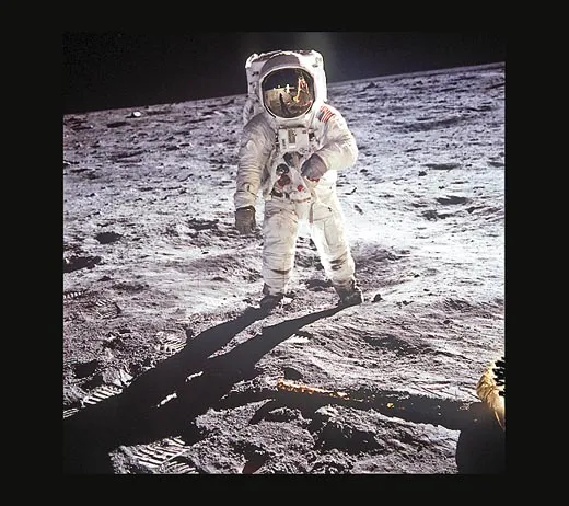 Photo shows Aldrin standing on moon, facing camera head on. You can see his whole spacesuit shining brightly. The reflection on his screen is shiny too.