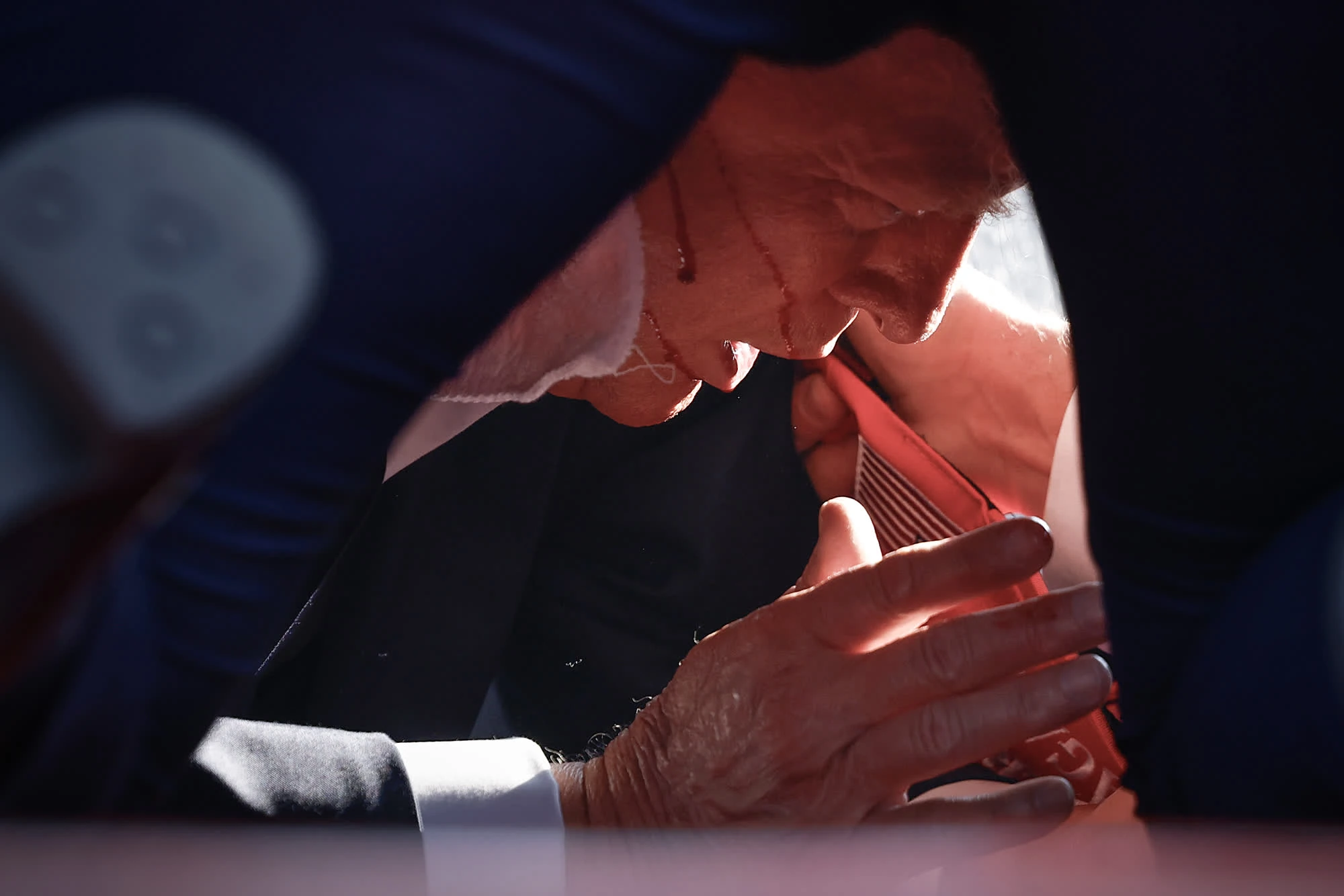 Photo shows Trump laying on floor with blood dripping down his face from his grazed ear. He has a shocked expression on his face.
