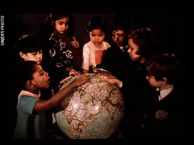 Photo shows a group of kids looking at the countries on a big globe.