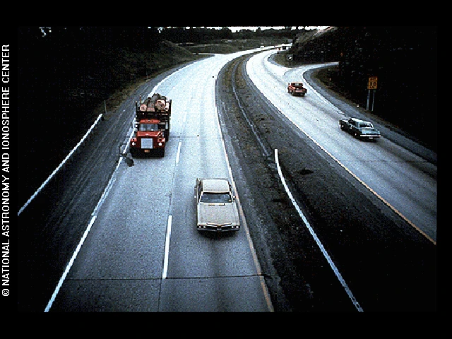Photo shows a highway with a car and a truck speeding down it.
